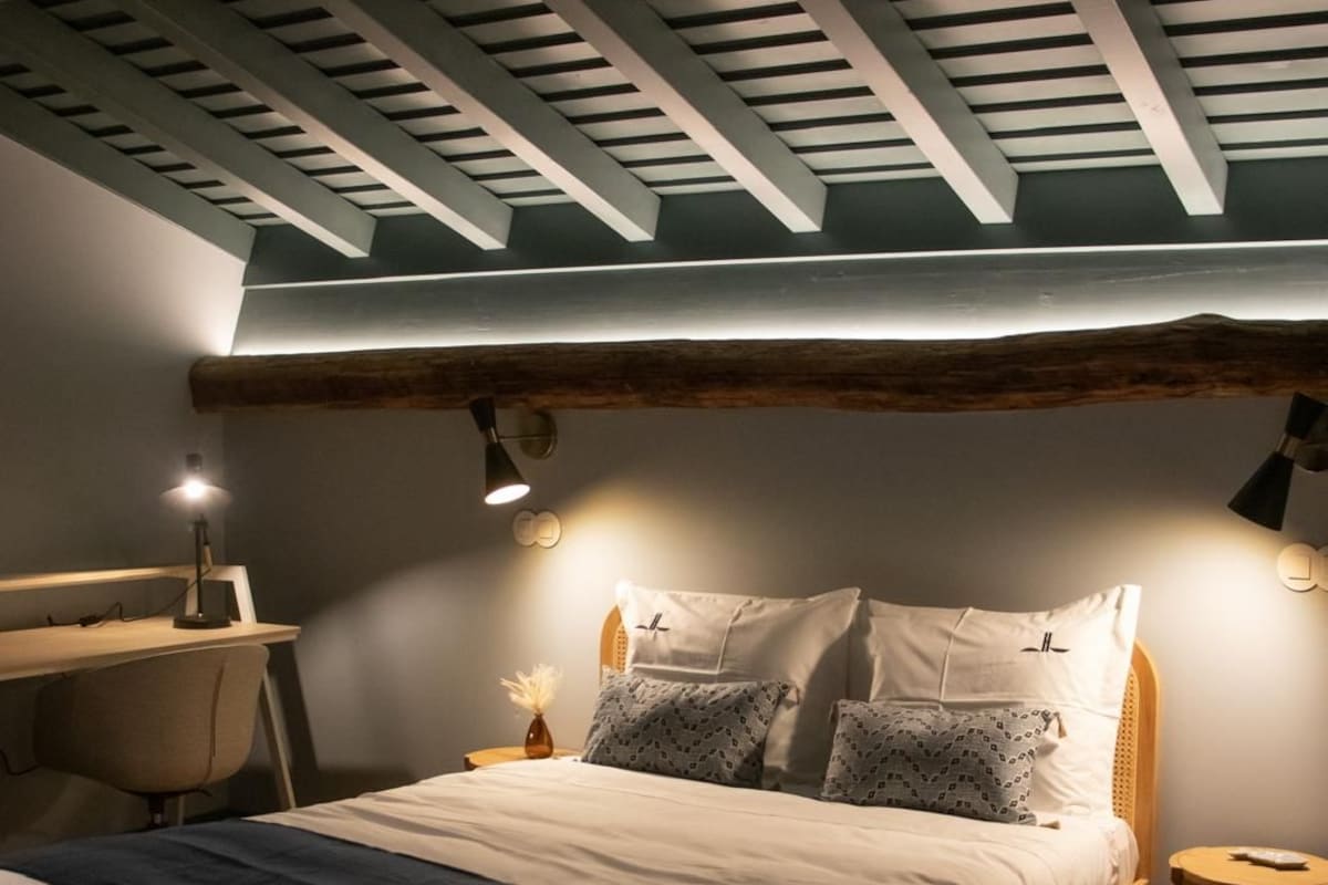 A bedroom with a sloped ceiling, a bed with multiple pillows, a desk, and a chair.