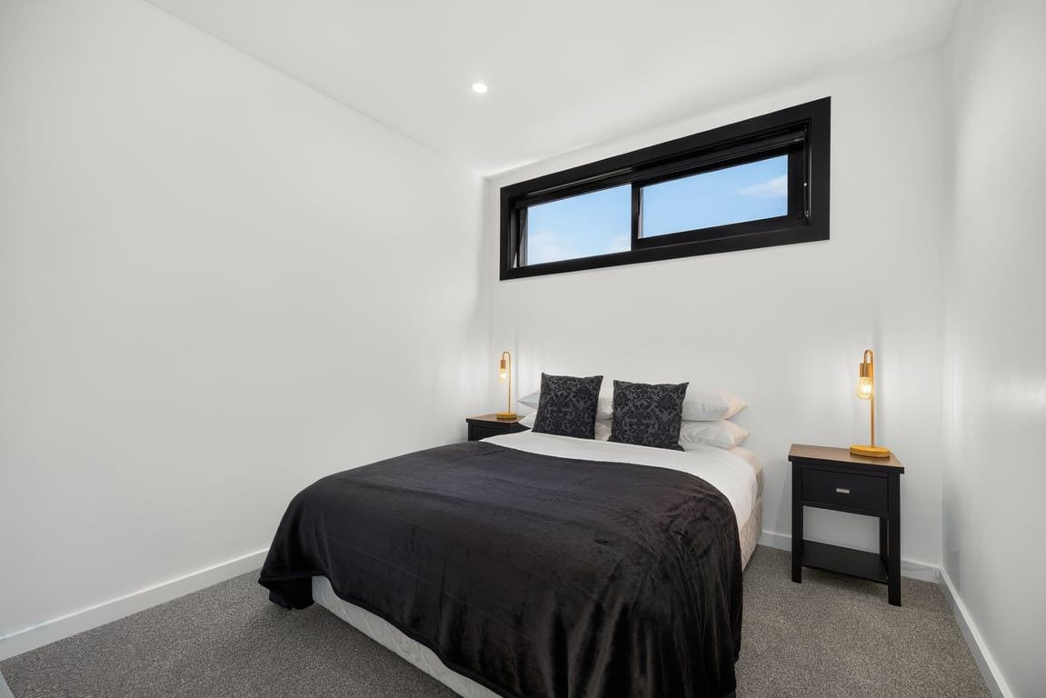 A bedroom with a bed, two bedside tables, a window, and a nightstand.