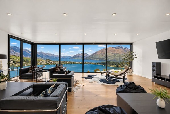 Una sala de estar moderna con un ventanal grande que da a un lago y montañas.