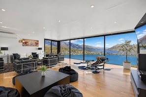 Una sala de estar moderna con un amplio ventanal con vistas a un lago y montañas.