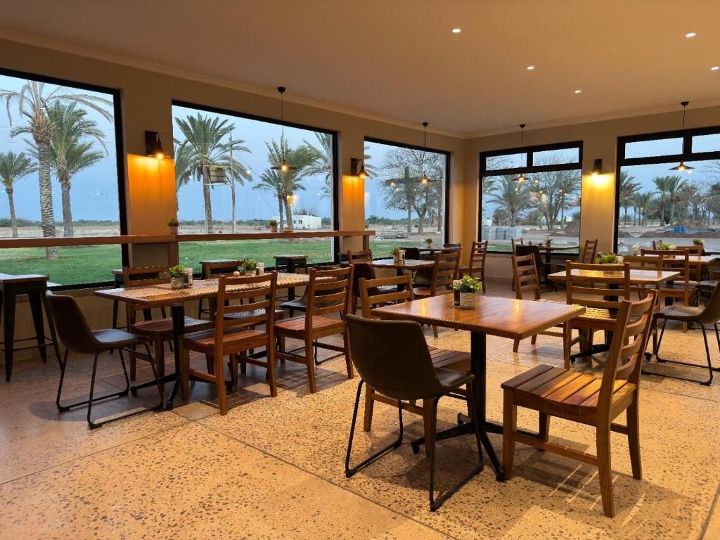 Un comedor amplio con varias mesas y sillas, ventanas grandes que dan a vistas de palmeras e iluminación colgante.