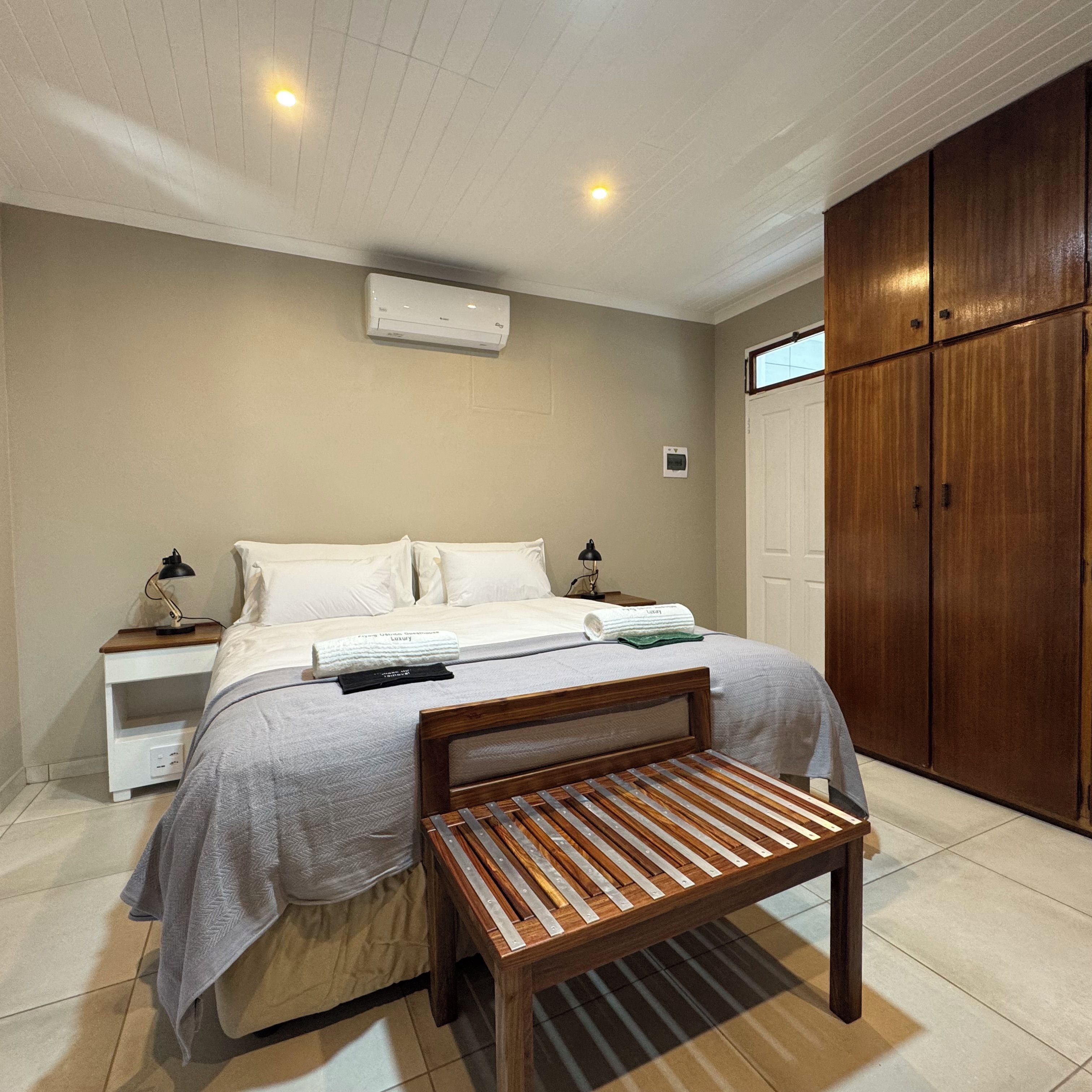 Un dormitorio con cama, mesitas de noche, equipo de aire acondicionado, armario y banca de madera.