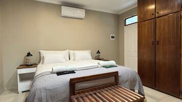 Un dormitorio con cama, mesitas de noche, equipo de aire acondicionado, armario y banca de madera.