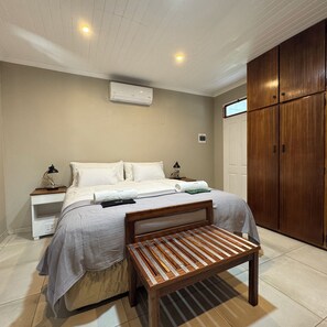 Ein Schlafzimmer mit einem Bett, Nachttischen, einer Klimaanlage, einem Kleiderschrank und einer Holzbank.