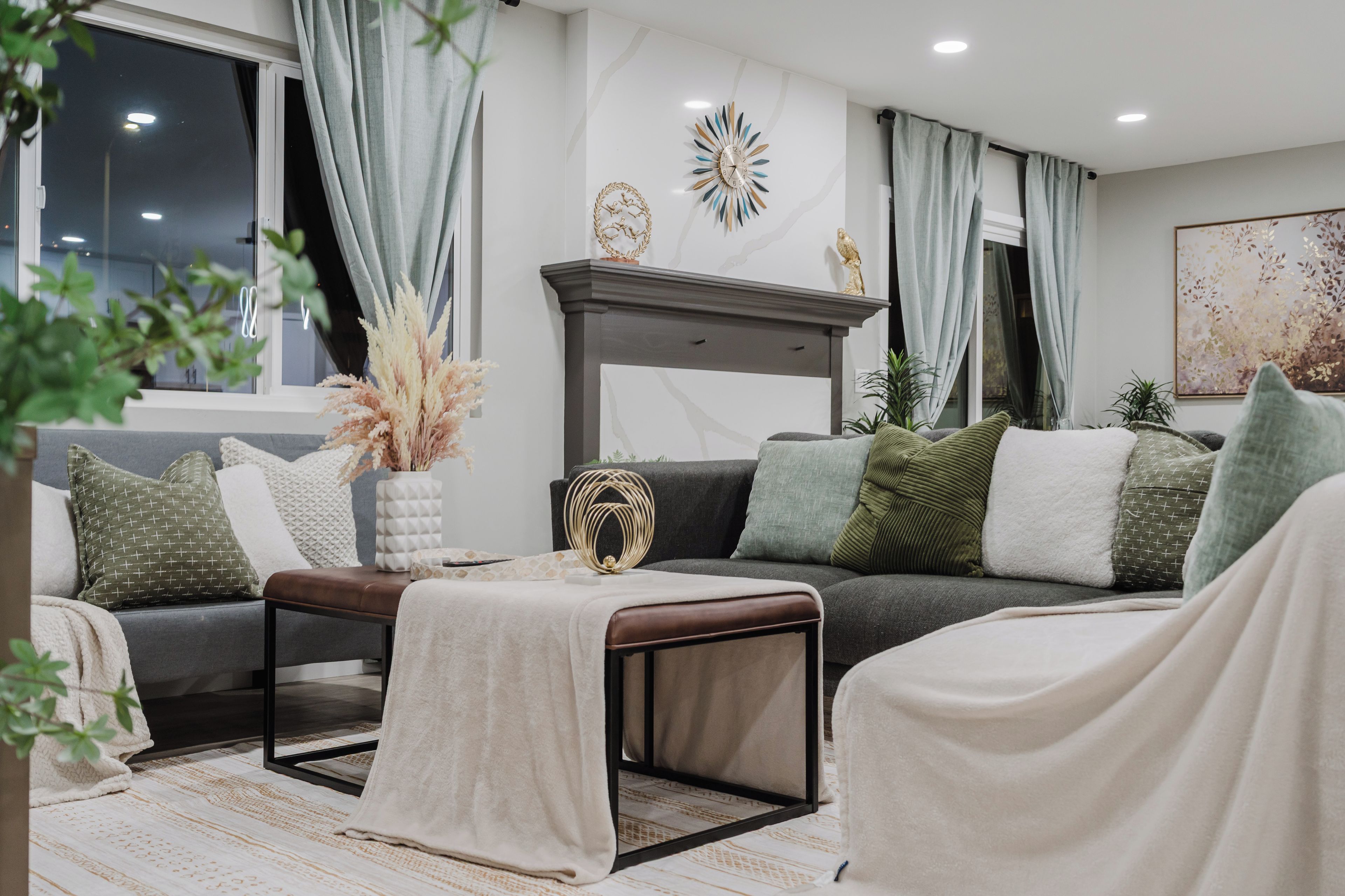 A modern living room with a grey sofa, a coffee table, and decorative pillows. There is a fireplace with a mantel and a wall clock.