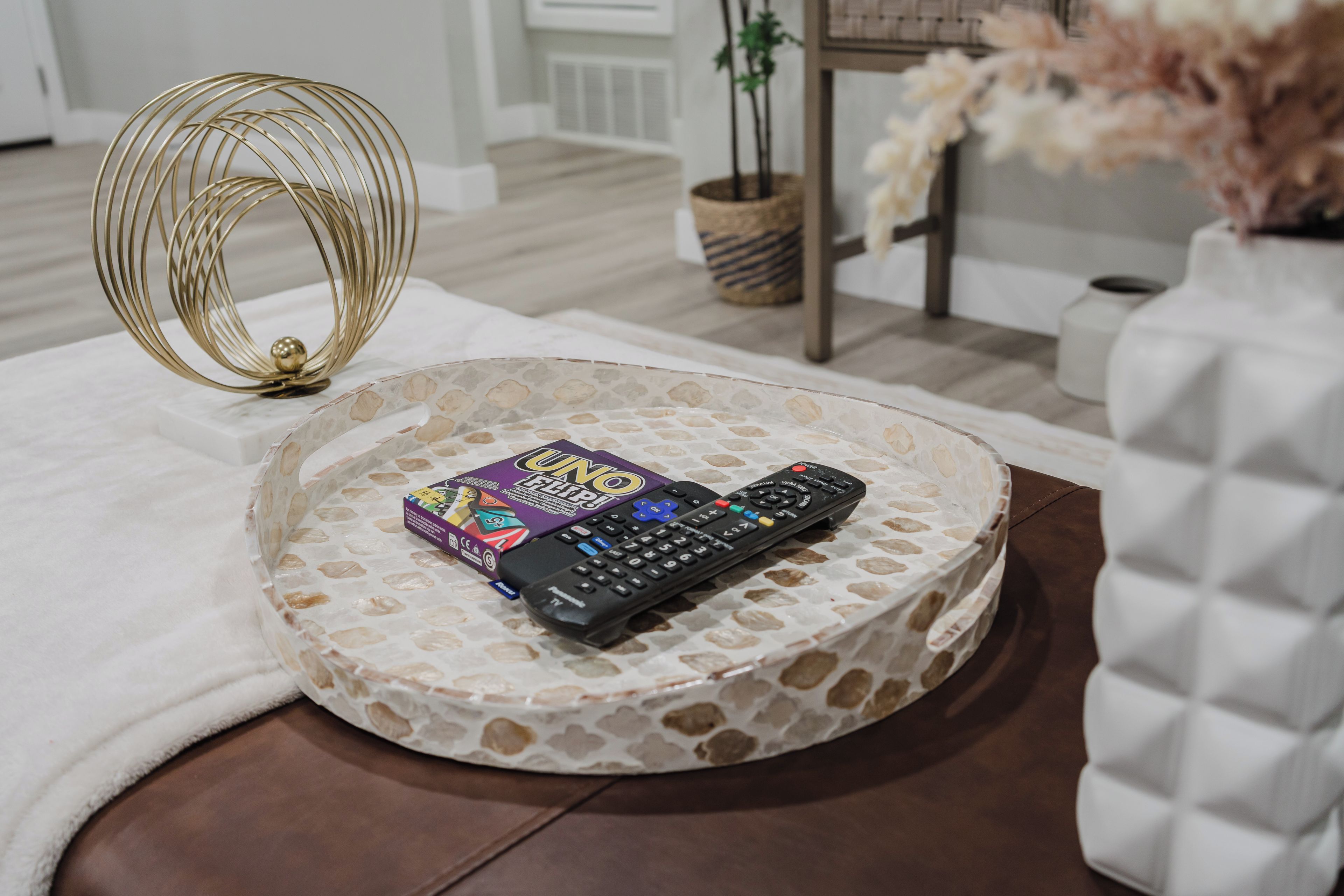 A round, stone-patterned tray with a remote control and a UNO game box on a white rug.