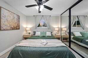 A bedroom with a large bed, two bedside tables, a ceiling fan, and a window with curtains.