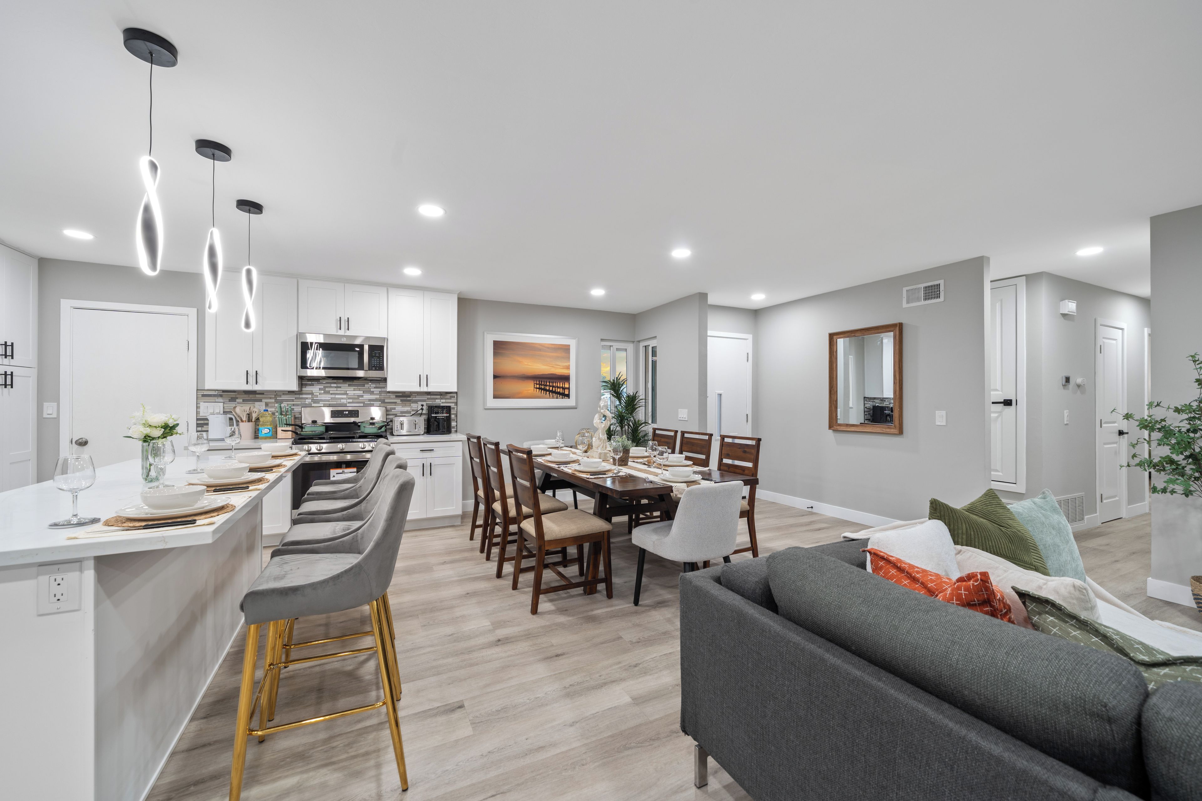 A modern kitchen with a central island, dining area with chairs, and a living room with a sofa.