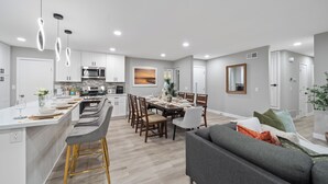 Et moderne køkken med en central ø, spiseområde med stole og en stue med sofa.