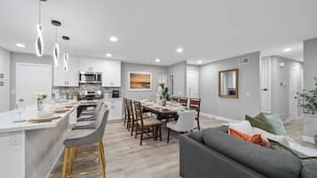 A modern kitchen with a central island, dining area with chairs, and a living room with a sofa.