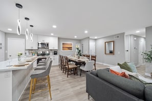 A modern kitchen with a central island, dining area with chairs, and a living room with a sofa. - Hot Tub, King Bed, Garage, Gated Yard, Ranch-Style (Spring Valley)