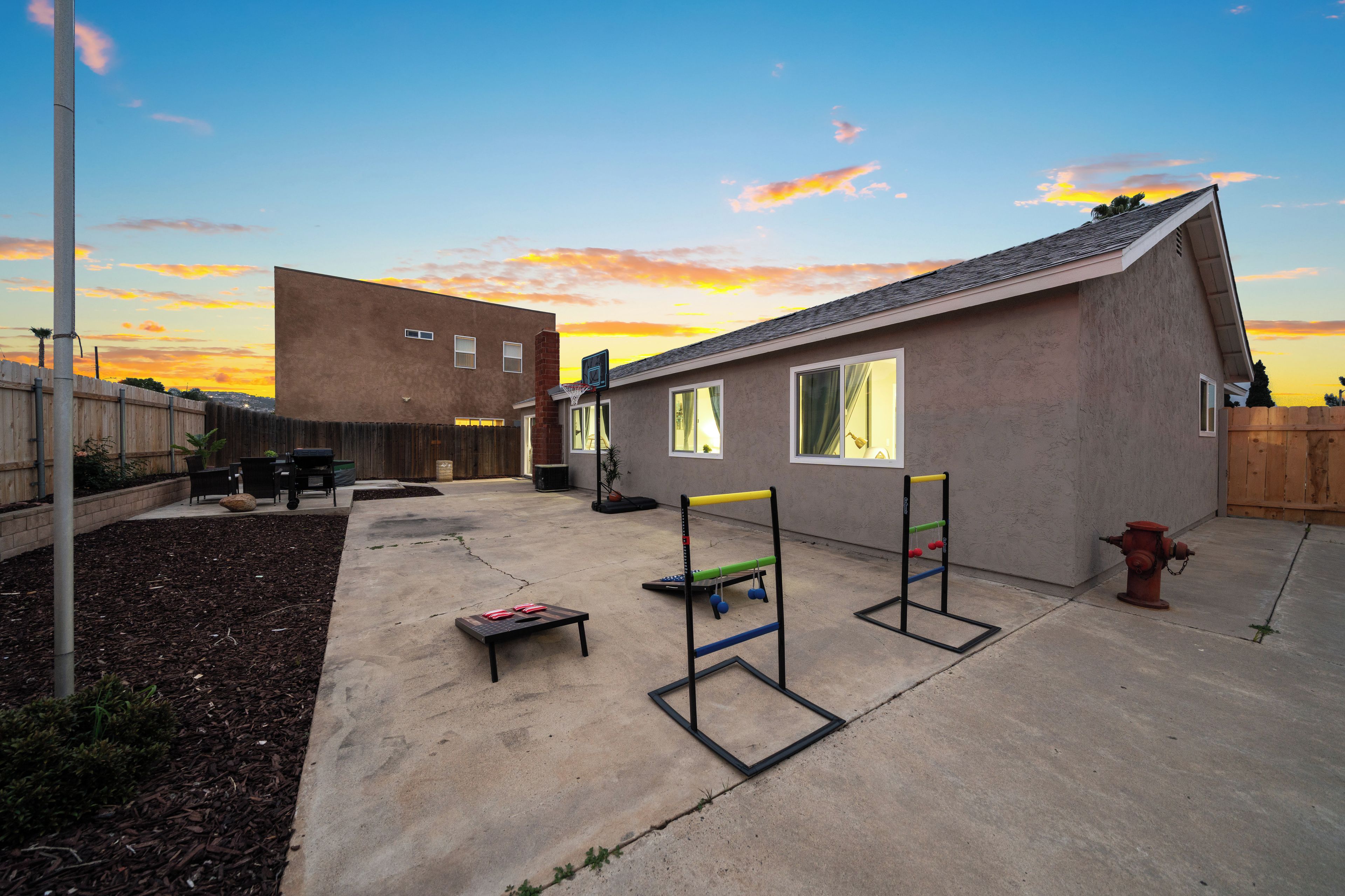 A backyard with a concrete patio, a basketball hoop, a small table, and a fire hydrant.