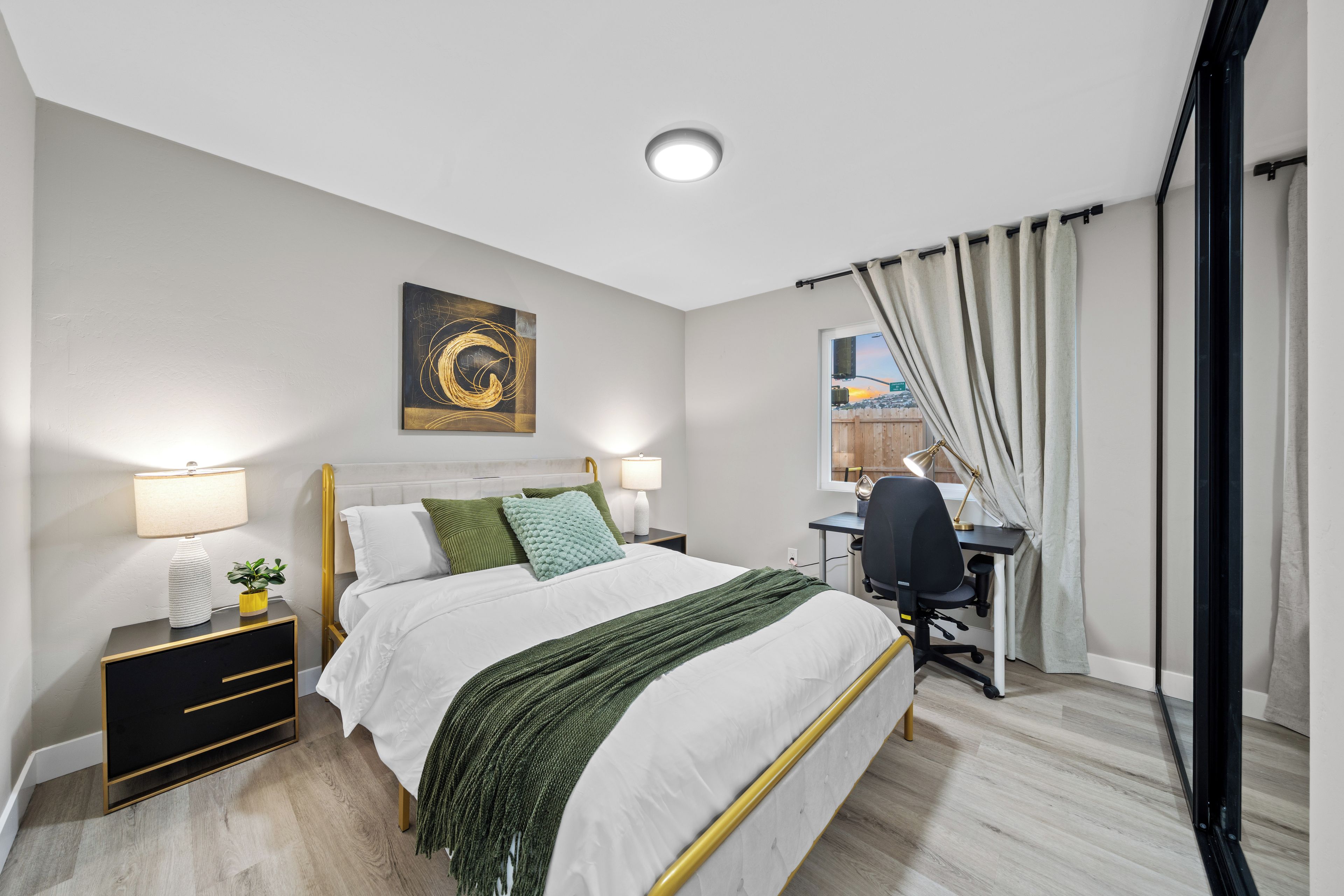 A bedroom with a bed, bedside tables, a desk, and a window with curtains.