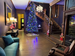 A cozy living room with a wooden staircase, a Christmas tree, and a fireplace.