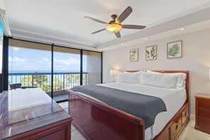 A hotel room with a bed, a desk, a balcony with a view of the ocean, and a ceiling fan. - ~NEW~ Modern Oceanfront at Waikiki Beach Tower (Honolulu)