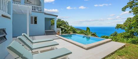 Une piscine avec vue sur l’océan, un patio couvert avec des chaises longues et un bâtiment doté d’un balcon.