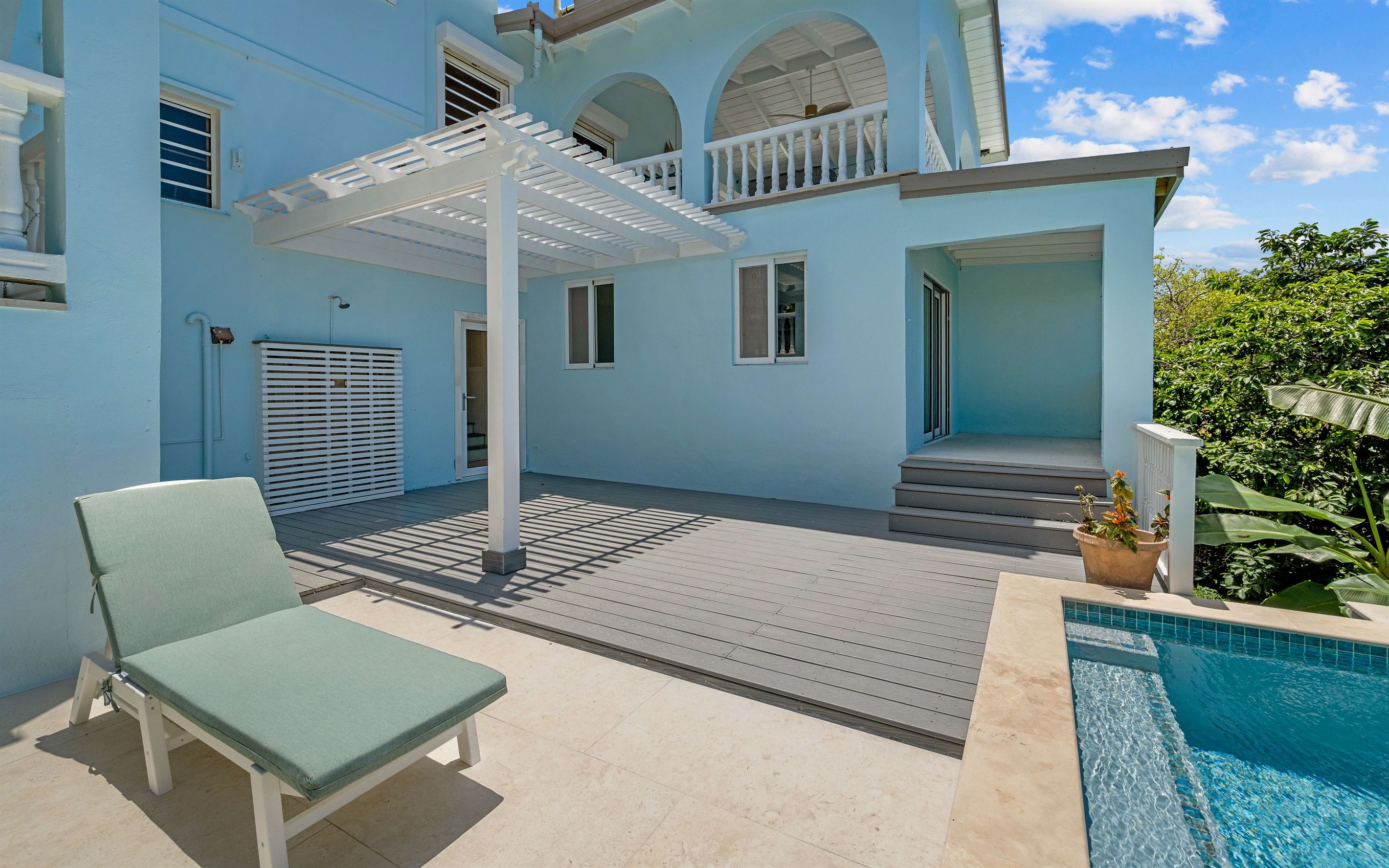 Un área junto a la piscina con una zona de estar cubierta, una escalera que lleva al segundo piso y una piscina.