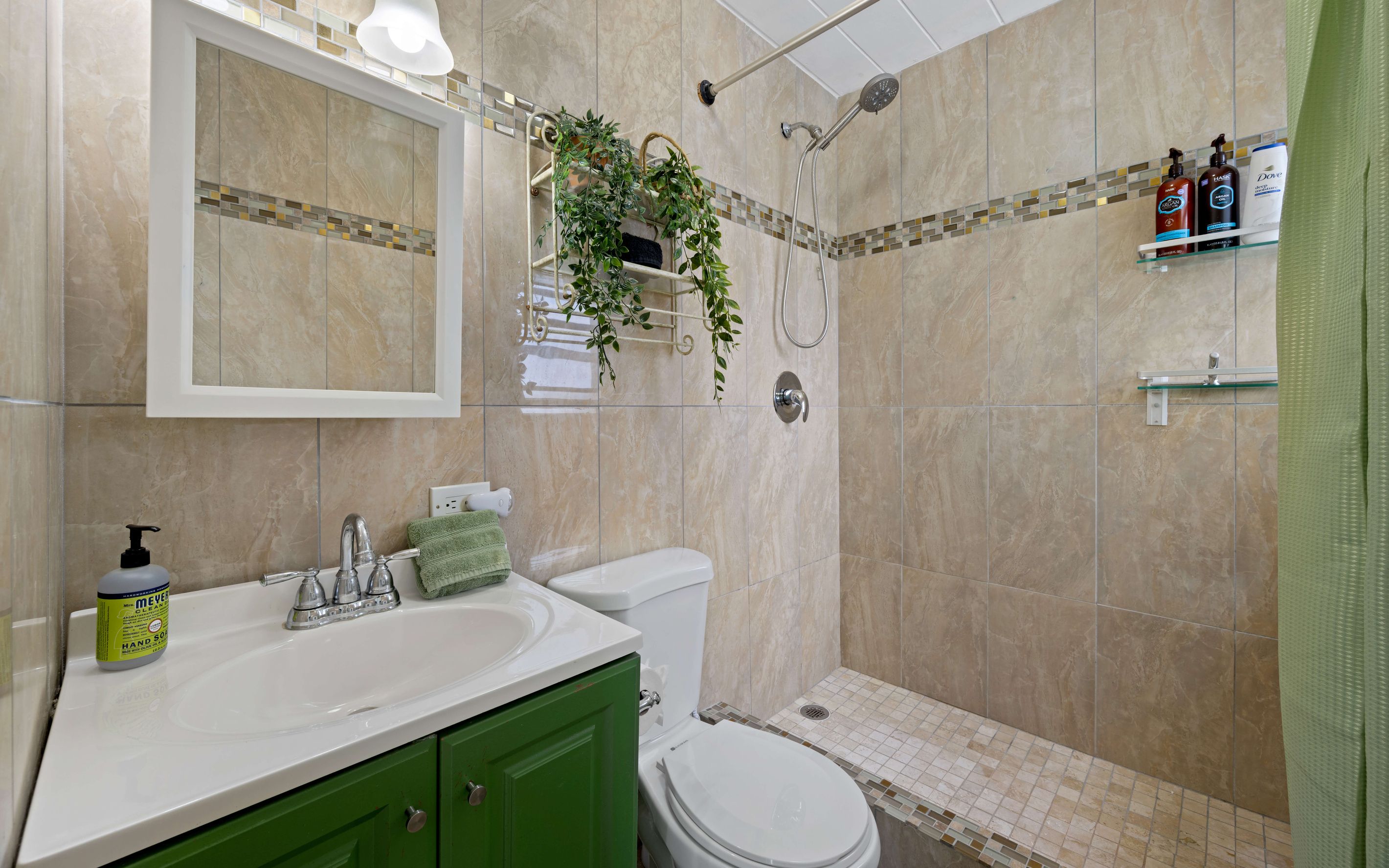 Un baño con un lavamanos blanco, armarios verdes, un inodoro, una ducha con puerta de cristal y un espejo sobre el lavamanos.