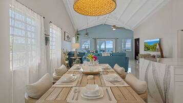 A dining area with a wooden table set for four, a blue sofa, and a view of the sea.