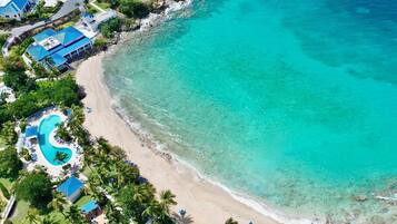 An aerial view of a coastal resort with a clear turquoise sea, a sandy beach, and a swimming pool.