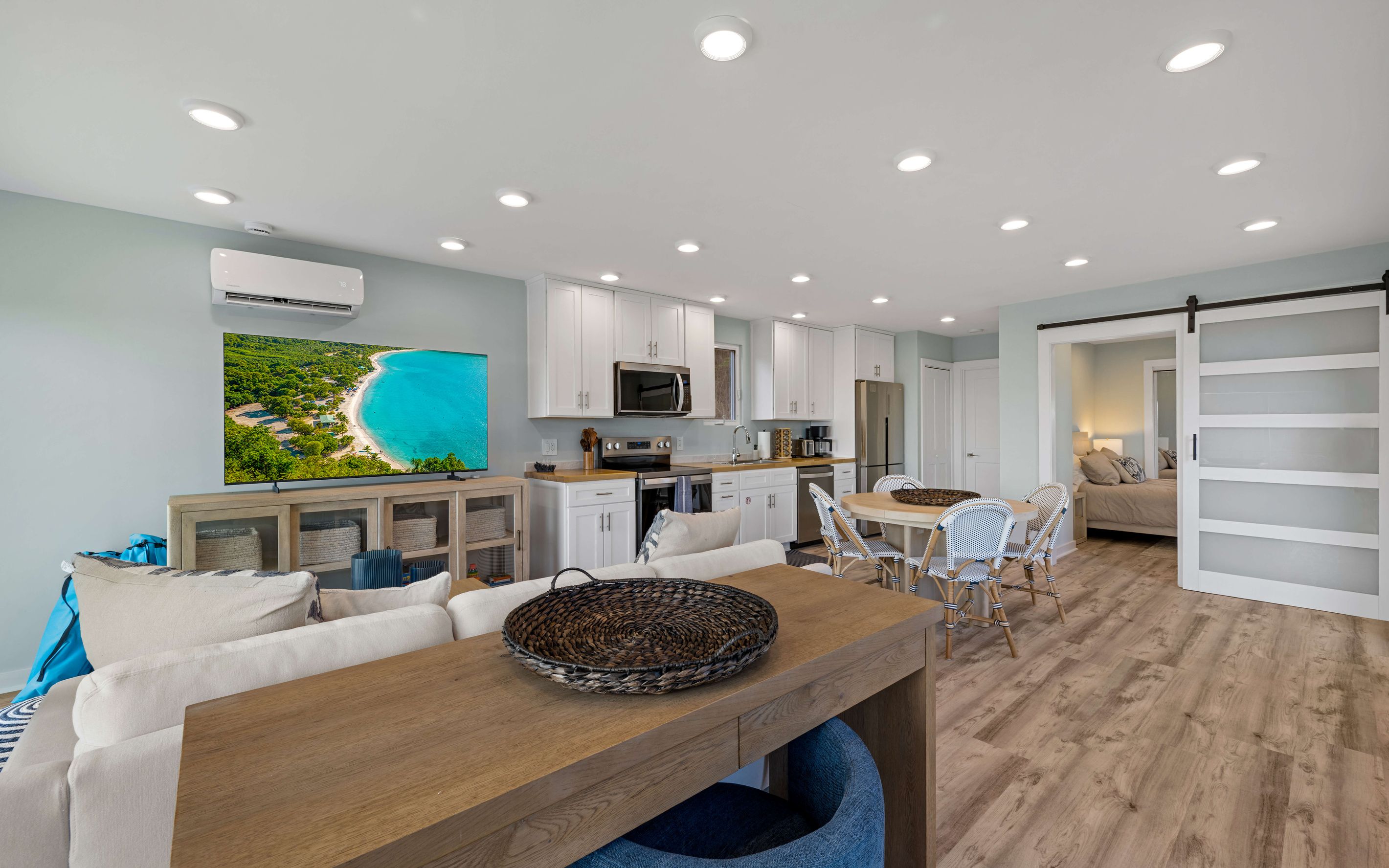 A modern kitchen with white cabinets, a large flat-screen TV, and a dining area with a wooden table and chairs.