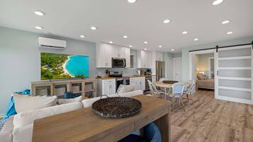 A modern kitchen with white cabinets, a large flat-screen TV, and a dining area with a wooden table and chairs.