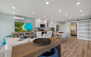 Une cuisine moderne avec des meubles blancs, un grand téléviseur à écran plat et un coin repas comprenant une table et des chaises en bois.