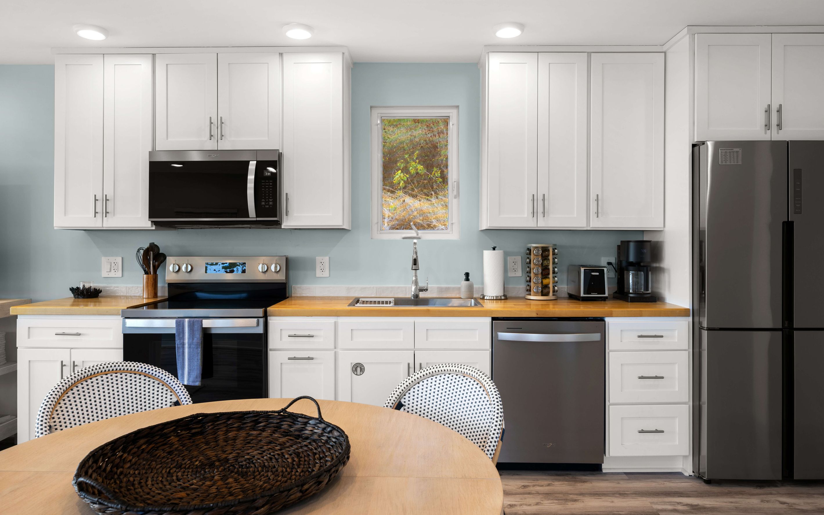 A modern kitchen with white cabinetry, a stainless steel refrigerator, a microwave, an oven, and a coffee maker.
