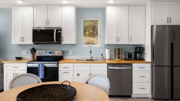 A modern kitchen with white cabinetry, a stainless steel refrigerator, a microwave, an oven, and a coffee maker.