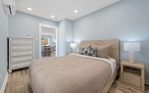 Une chambre avec un grand lit, des lampes de chevet, une commode et une vue sur la salle à manger.