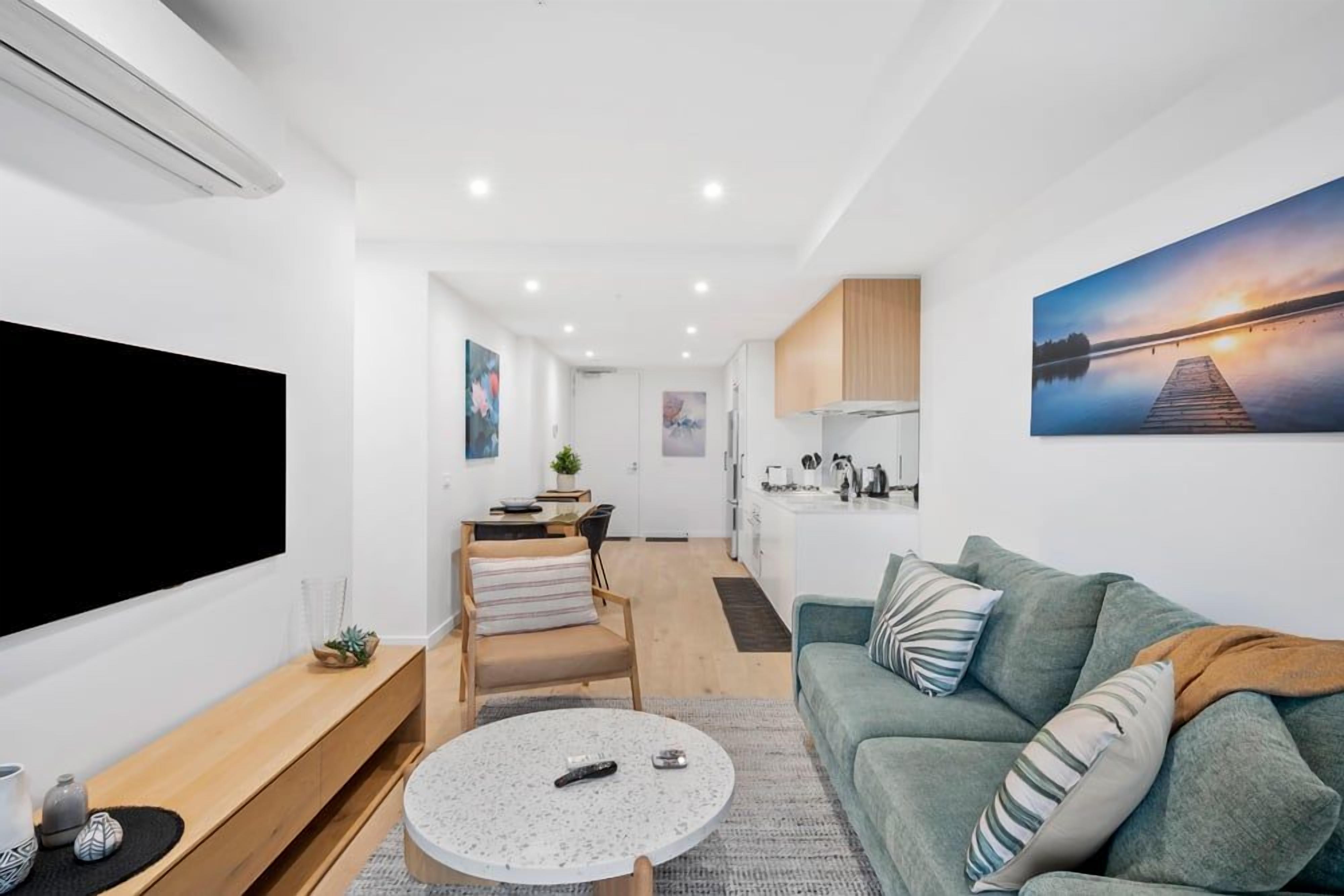 A modern living space with a flat-screen TV, a sofa, a coffee table, and a kitchen area.