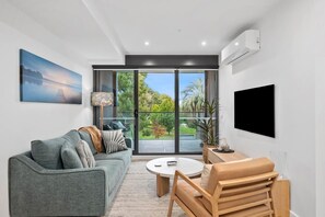 Ein modernes Wohnzimmer mit einem grauen Sofa, einem runden Couchtisch und einem an der Wand befestigten Fernseher.