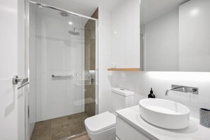 Ein modernes Badezimmer mit einer gläsernen Duschkabine, einem weißen Waschbecken und einer Toilette.