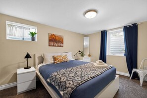 A bedroom with a bed, a bedside table, a lamp, a window with curtains, a plant, and a painting on the wall. - Hot Tub + Fire Pit + Movie Projector+ BBQ - Near DT Denver (Thornton)
