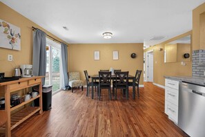 A compact kitchen with a dining area, wooden flooring, and a view through the window. - Hot Tub + Fire Pit + Movie Projector+ BBQ - Near DT Denver (Thornton)
