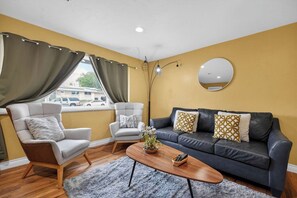 A living room with a sofa, two armchairs, a coffee table, and a large mirror on the wall.
