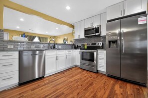A modern kitchen with stainless steel appliances, white cabinetry, and a wooden floor.