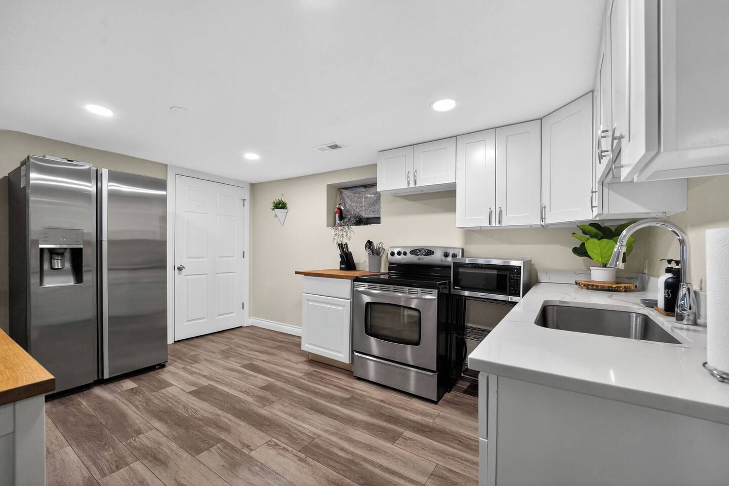 A modern kitchen with stainless steel appliances, white cabinetry, and a wooden floor.