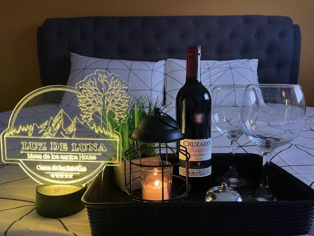 A bed with a headboard, a bottle of wine, two glasses, a candle, and a decorative sign.