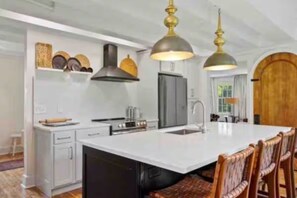 A kitchen with a large island, white cabinetry, and a wooden door. - 1865 Bennington Farmhouse: Mountain, Monument & Meadow views & Charm (Bennington)