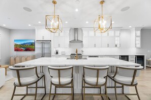 A modern kitchen with a large island, bar stools, and pendant lighting. - Sunset Island 3B Hidden Cove Way (Ocean City)
