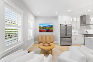 A modern kitchen with white cabinetry, stainless steel appliances, and a view of a landscape painting. - Sunset Island 3B Hidden Cove Way (Ocean City)
