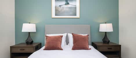 Una cama bien hecha con dos almohadas, cabecera y dos mesitas de noche con lámparas.