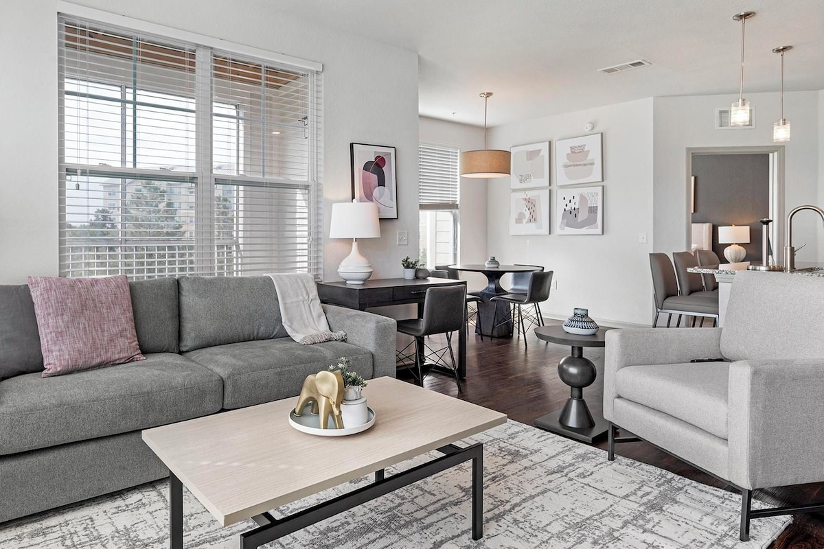 A modern living room with a grey sofa, a coffee table, and a dining area with a table and chairs.