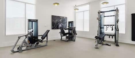 A gym with various exercise equipment, large windows, and a painting on the wall.