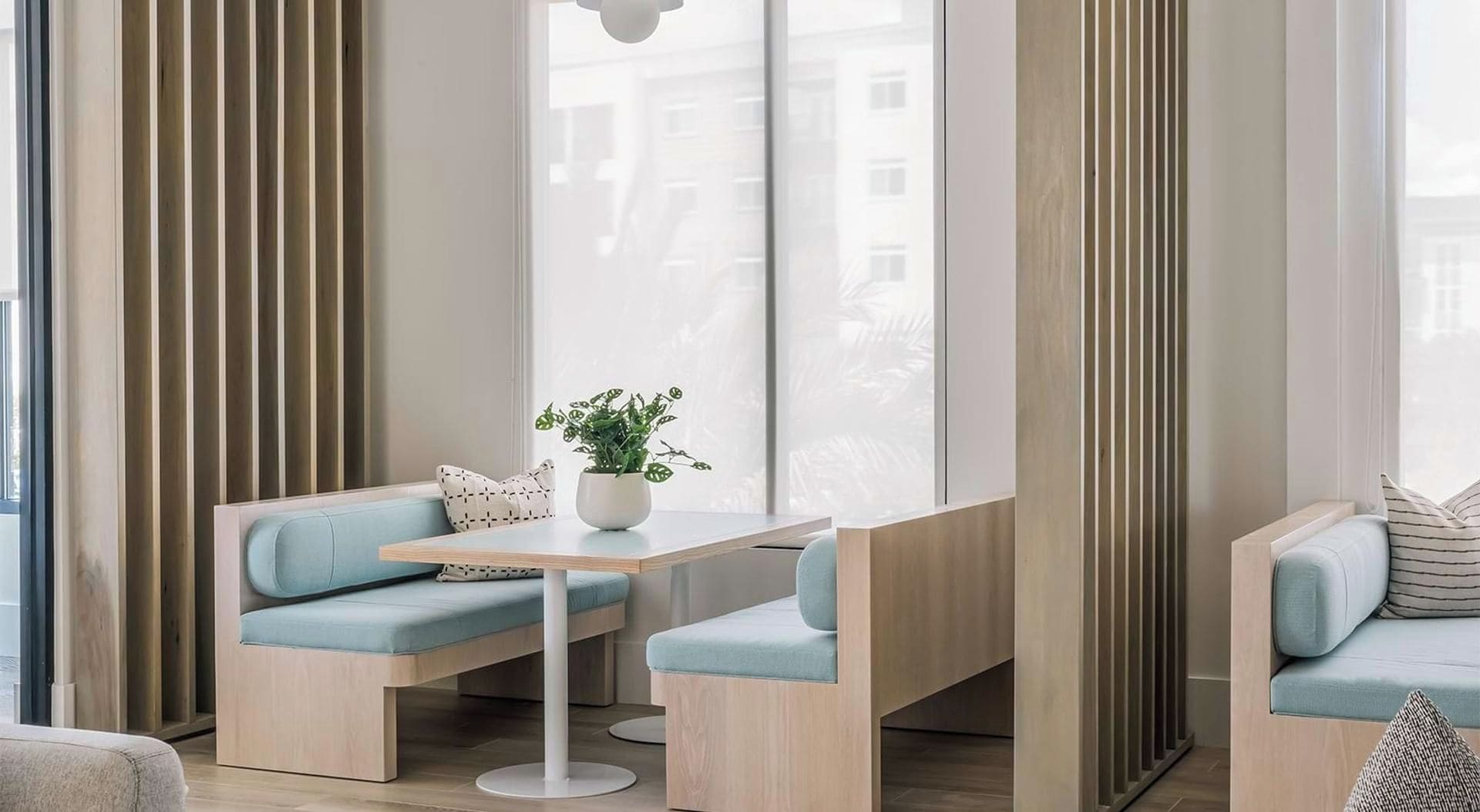 Een moderne zithoek met een tafel en stoelen, een potplant en een uitzicht door grote ramen.