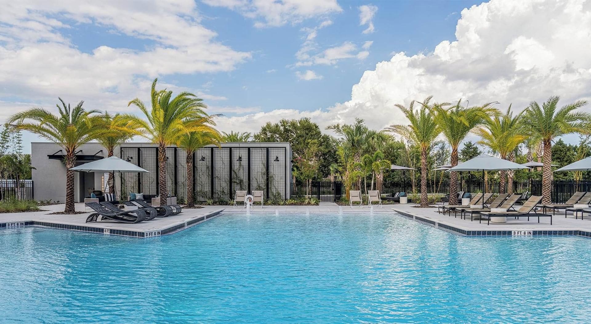 Une piscine entourée de palmiers et d’un bâtiment moderne, avec des chaises longues et des parasols à proximité.