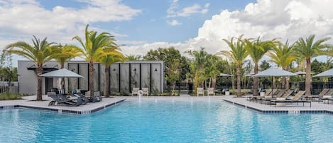 Une piscine entourée de palmiers et d’un bâtiment moderne, avec des chaises longues et des parasols à proximité.