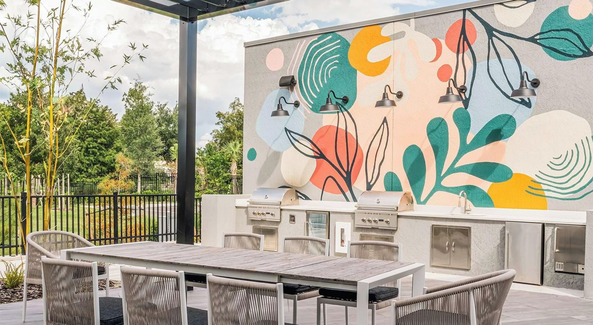 Um pátio externo com churrasqueira, mesa de jantar e cadeiras, e um mural abstrato e colorido na parede.