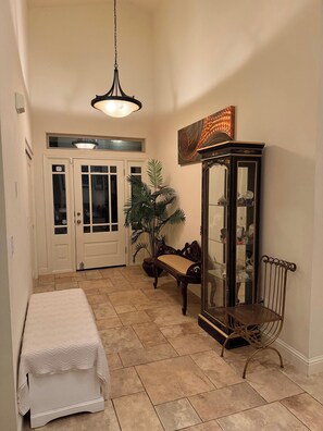 A hallway with a bench, a potted plant, a cabinet with glass doors, and a hanging light fixture.